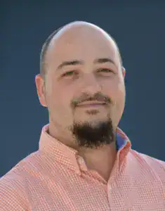 Portrait of Nate O'Neel in a pink checkered shirt with a blue background.