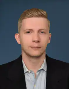 Professional headshot of a young man in a suit and light blue shirt.