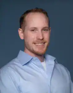 Professional headshot of a smiling man in a light blue shirt.