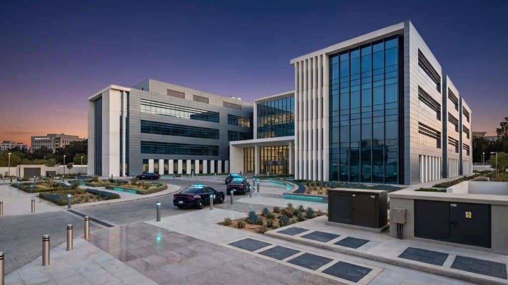 Modern corporate office building with glass facade and parking lot at sunset.